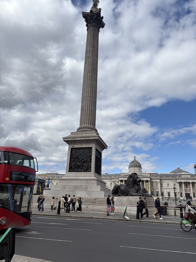 A red double-decker bus passing Nelson's Column in Trafalgar Square.